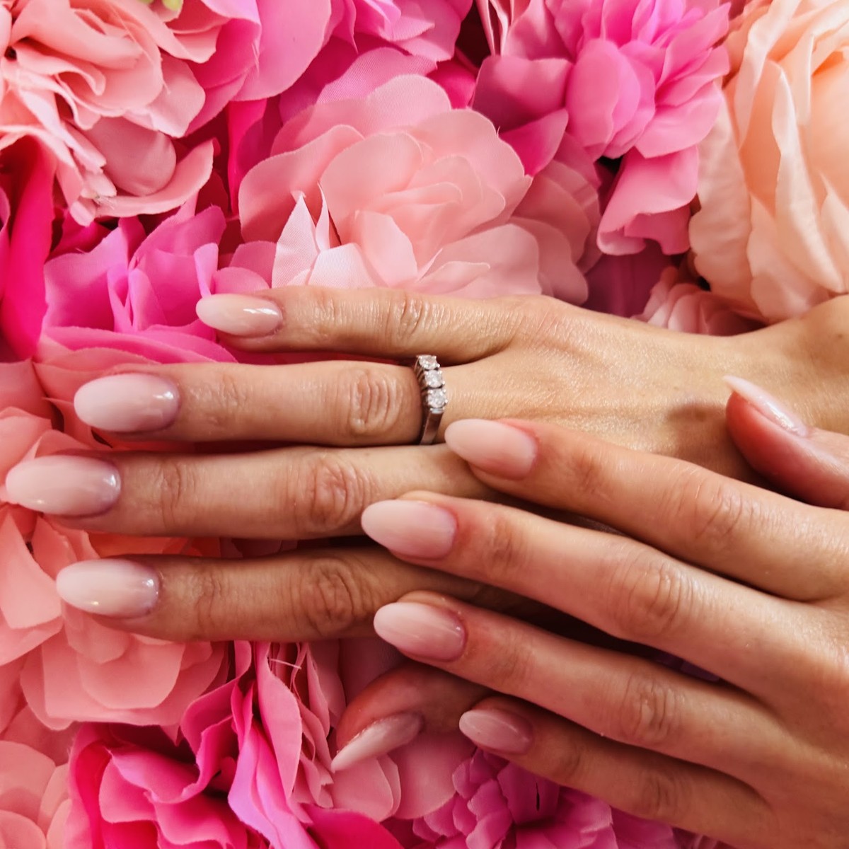 Nude amandelnagels tegen de bloemenwand in de salon