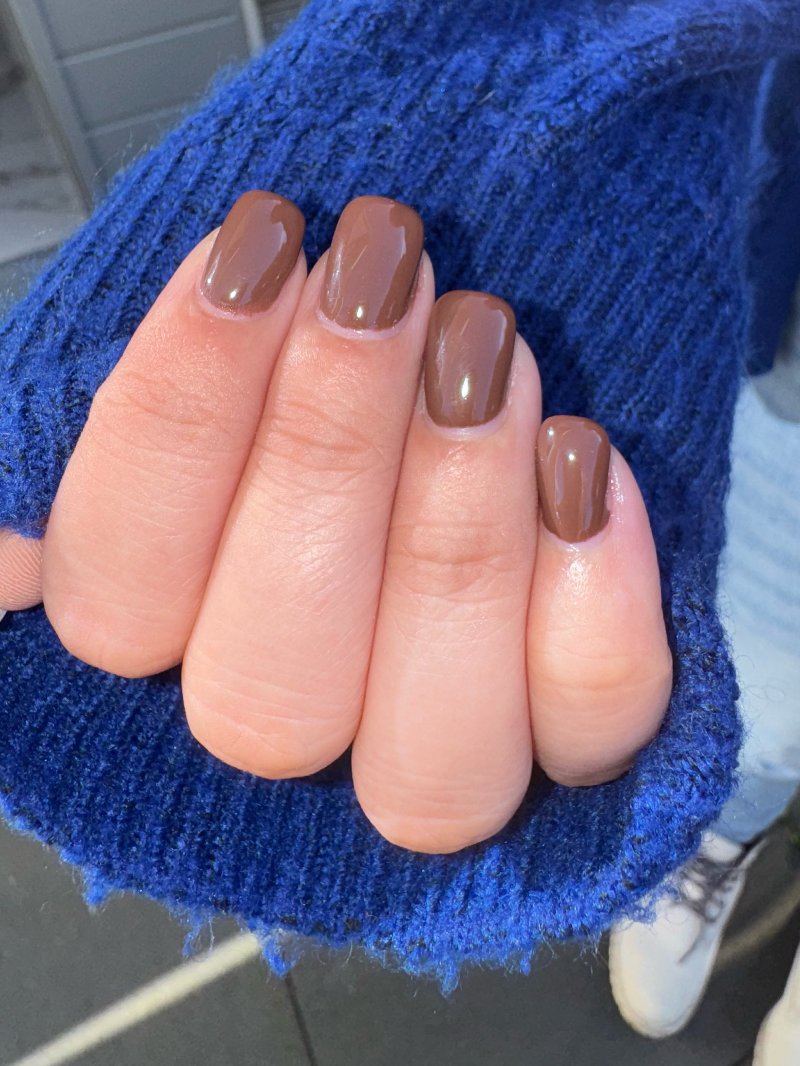 Mokkabruine nagels tegen een blauwe mouw